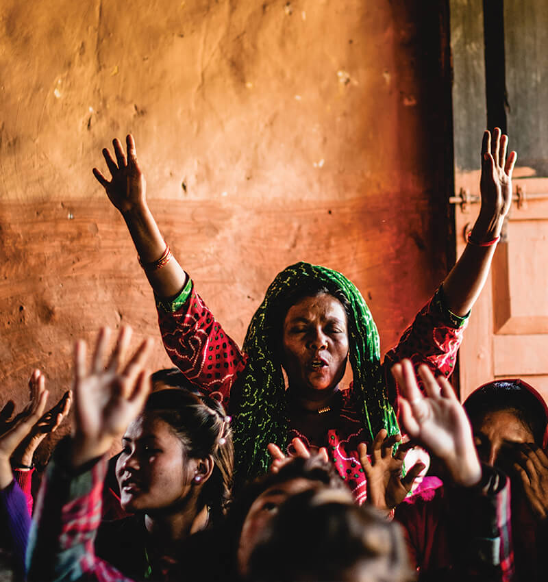 Close up of a woman in a group of people worshipping with her hands up