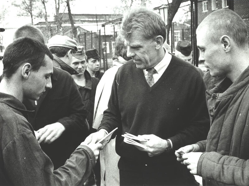 Black and white photo of a white man handing out pamphlets to people on a crowded sidewalk.