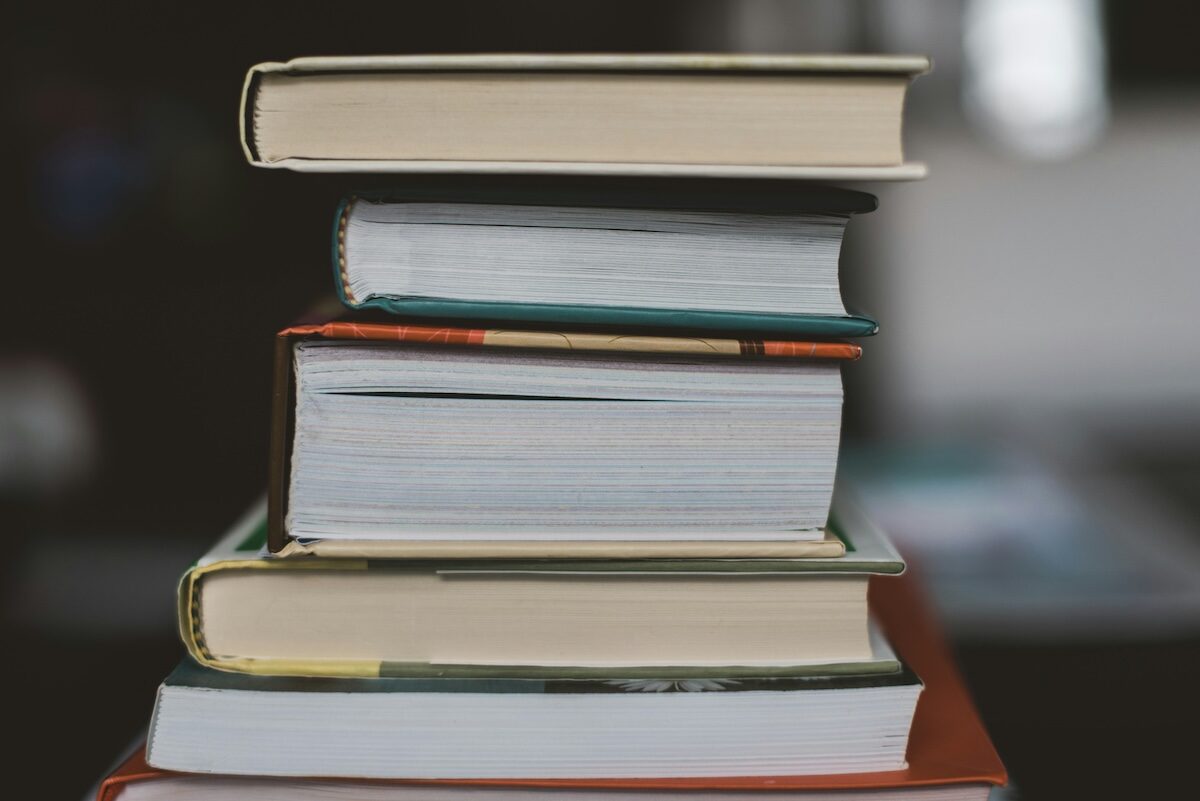 A stack of five hardcover and paperback books is shown, viewed from the side, with pages and covers visible.
