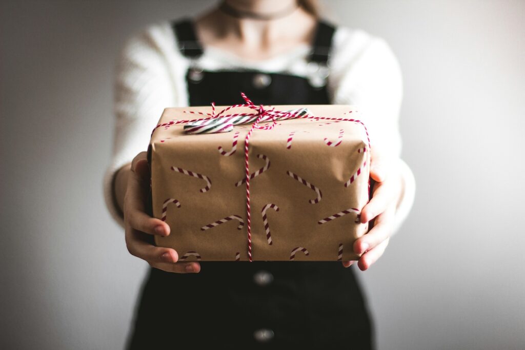 Person holding out a wrapped gift with brown paper and red-and-white string.