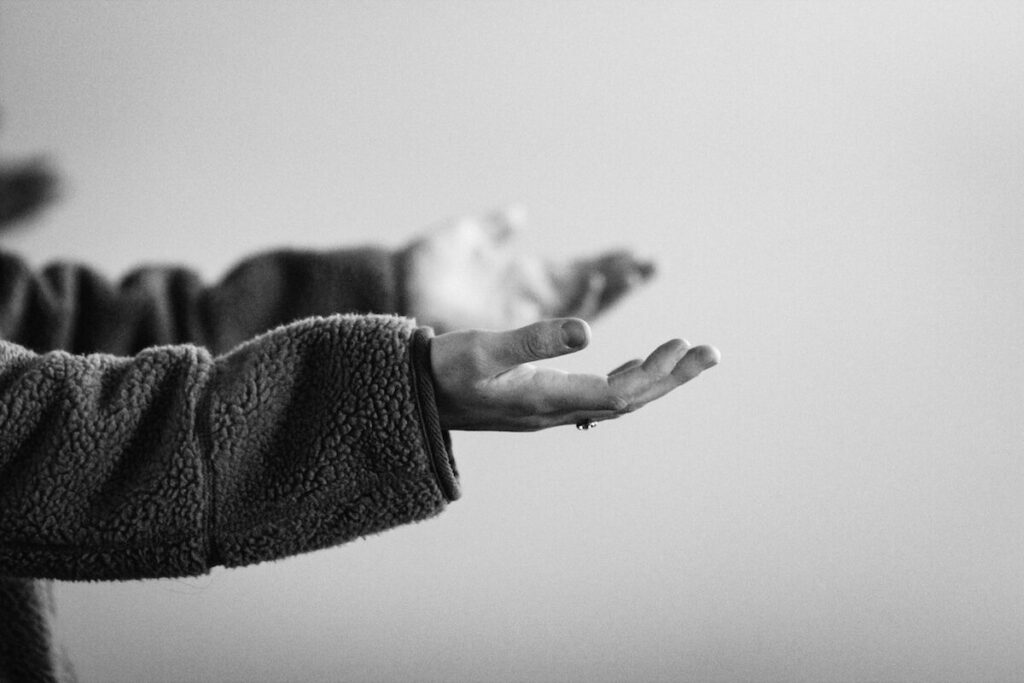 A person in a fleece jacket holds out their open hands, palms facing up, against a plain background.