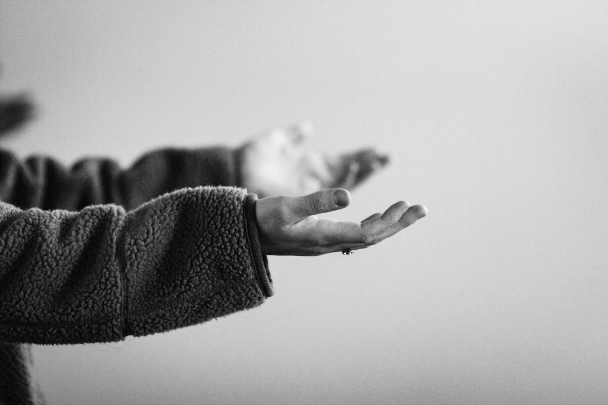 A person in a fleece jacket holds out their open hands, palms facing up, against a plain background.