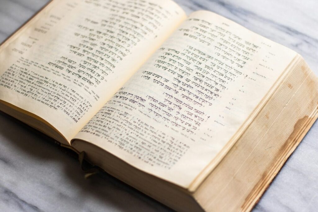 An open book with text in Hebrew script lies on a marble surface.