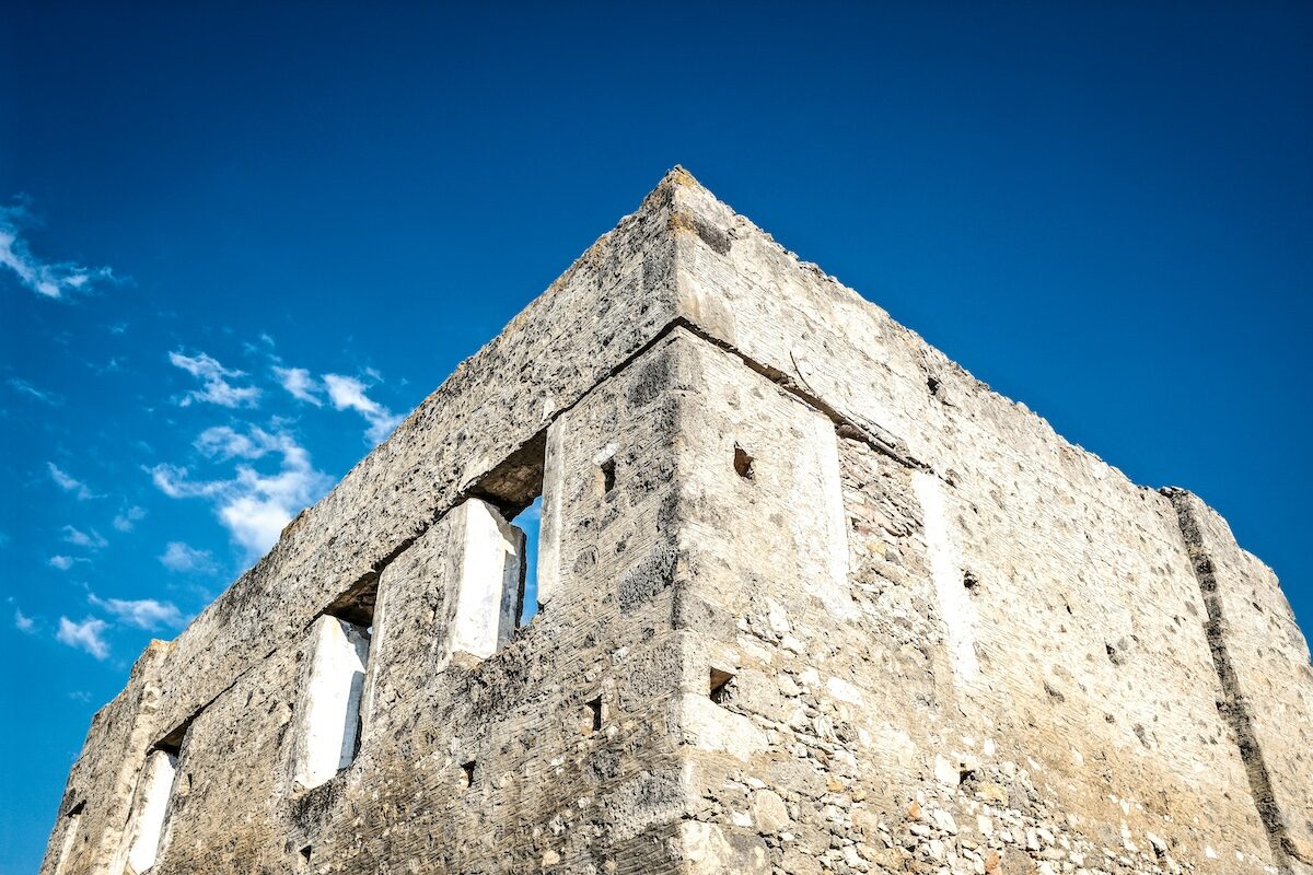 Stone wall ruins of an old building with three window openings, set against a clear blue sky with a few clouds.