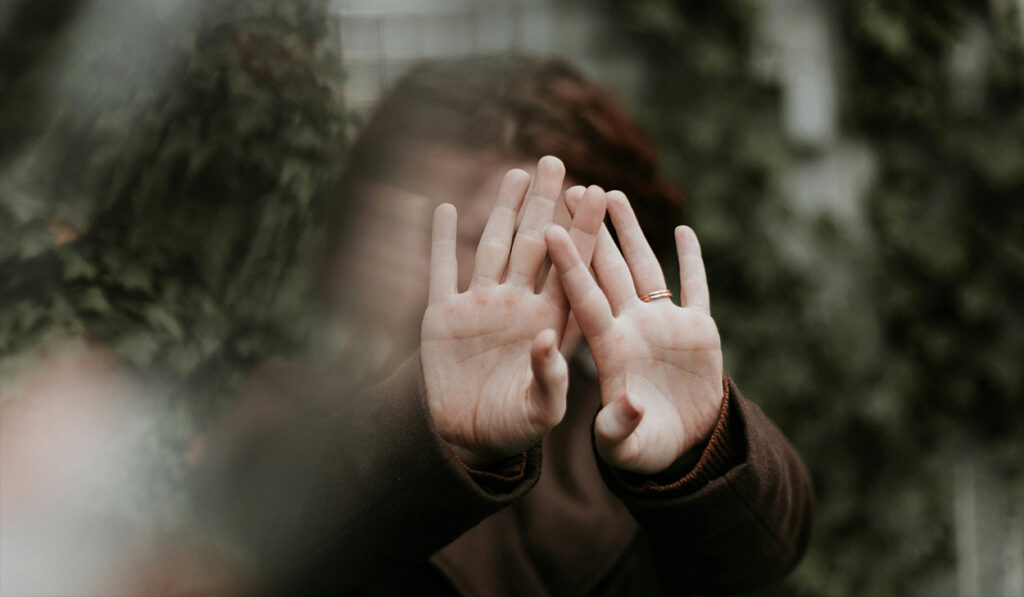 A woman holds up her hands to cover her face.