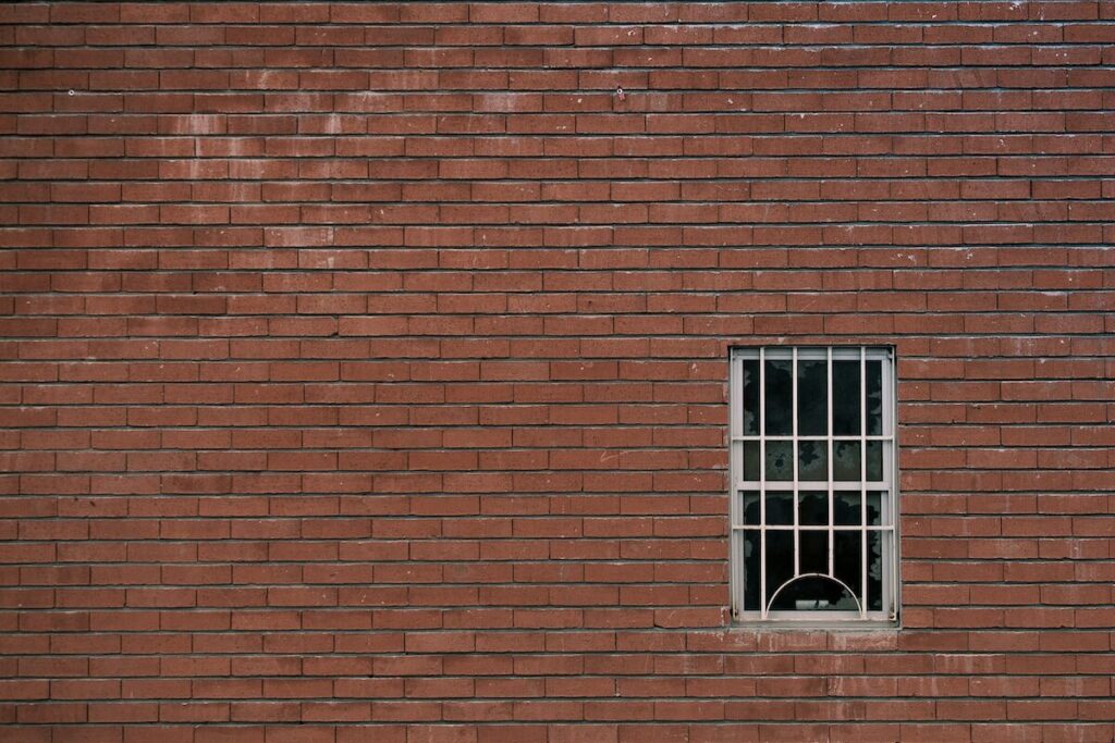 A small, barred window is set into a red brick wall. The window is located on the right side of the image.