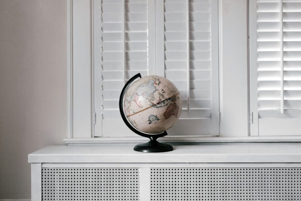 A globe with a black stand sits on a white surface in front of closed white window shutters.