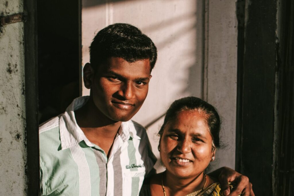 A young man and a woman standing closely together, smiling, at the entrance of a building.