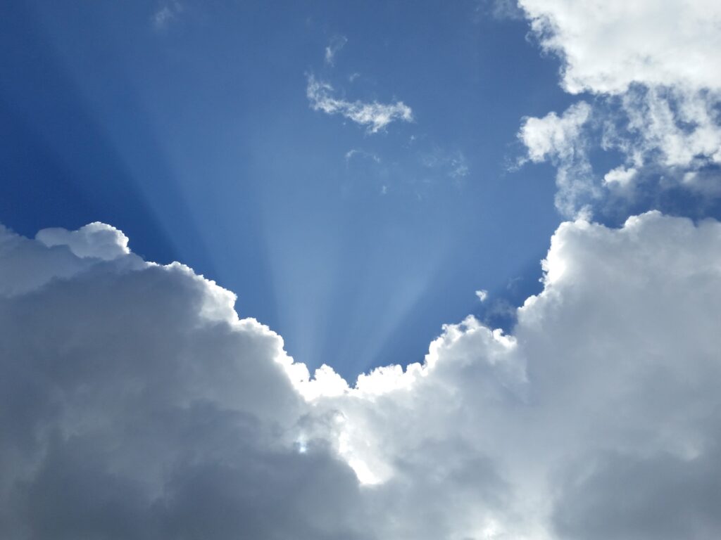 Sun rays shine through a gap between large, fluffy clouds against a blue sky.