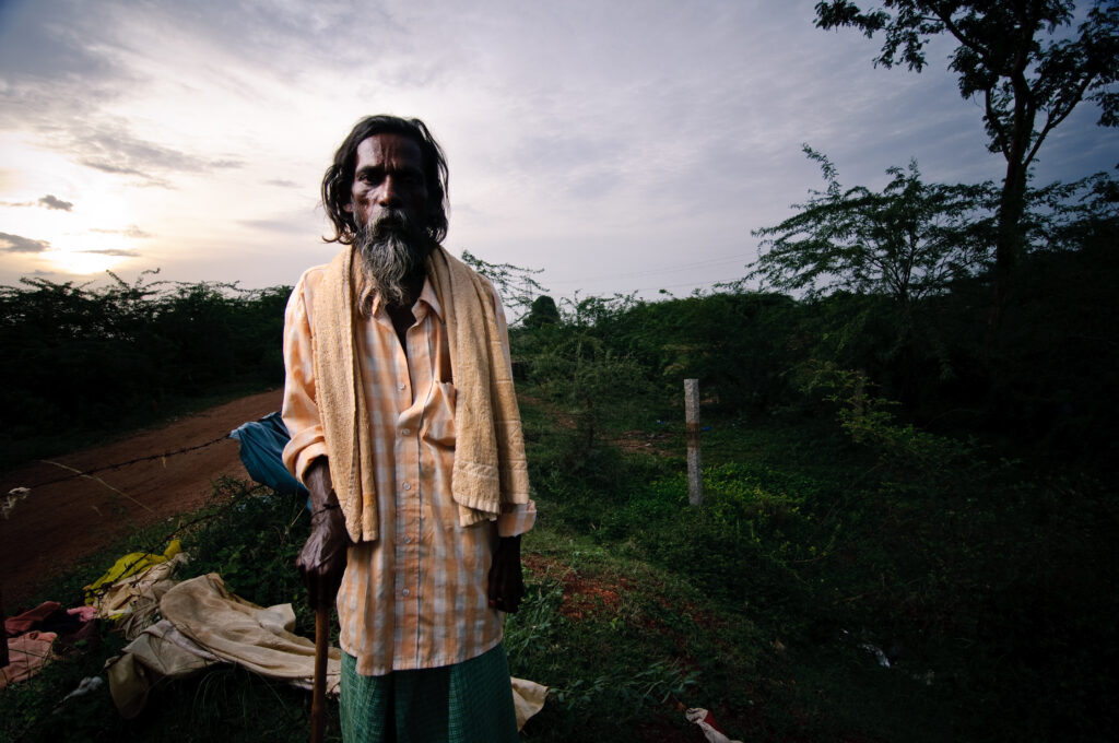 Elderly man in the middle of the jungle with an orange top with a cane