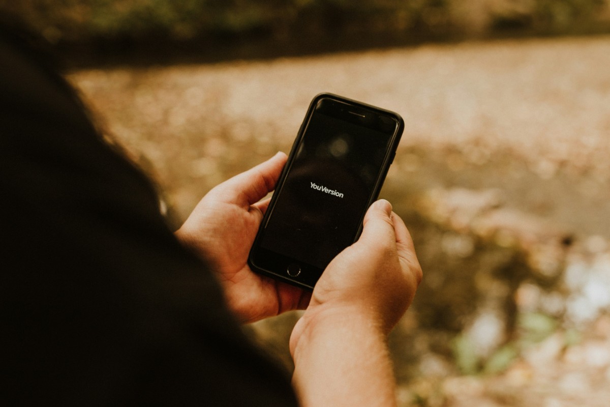 Person holding a smartphone displaying a loading screen with the Facebook logo, standing outdoors with a blurred natural background.