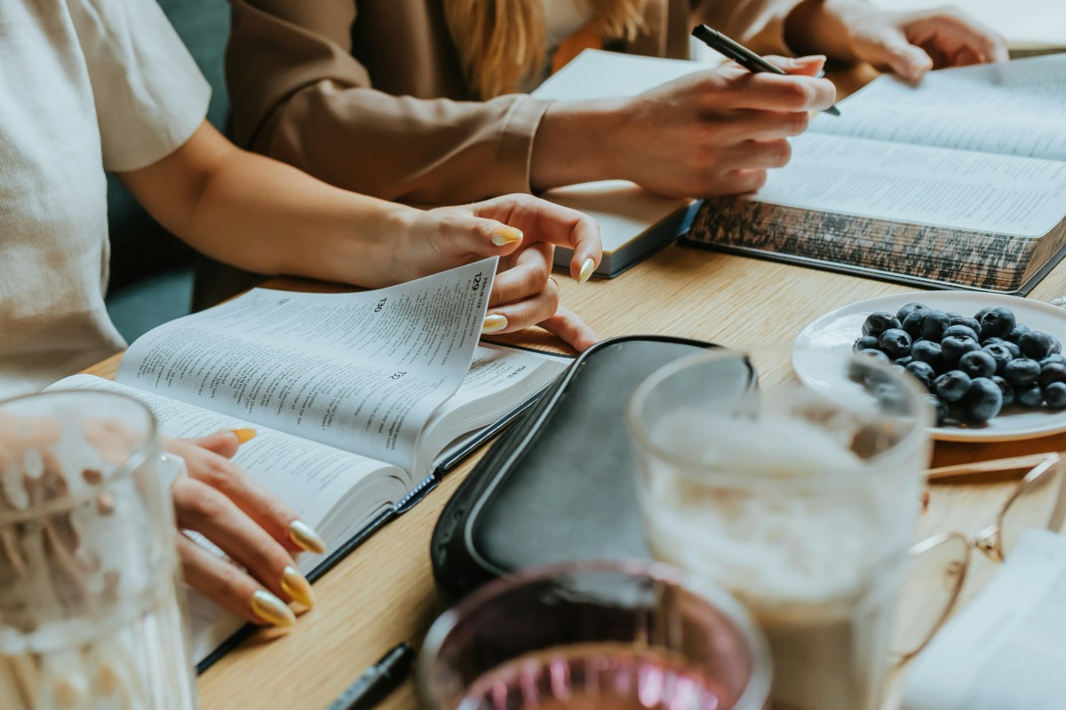 Three people studying at a table with open books, pens, and a plate of blueberries.