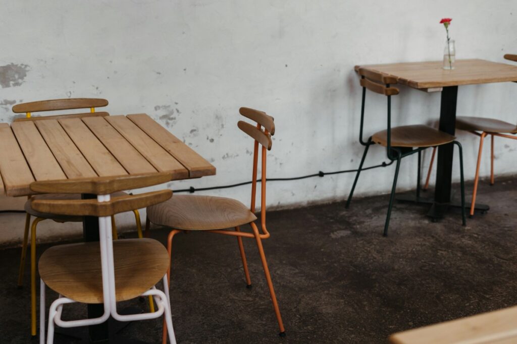 Two empty wooden tables with chairs in a cafe setting; one has a single flower in a vase.