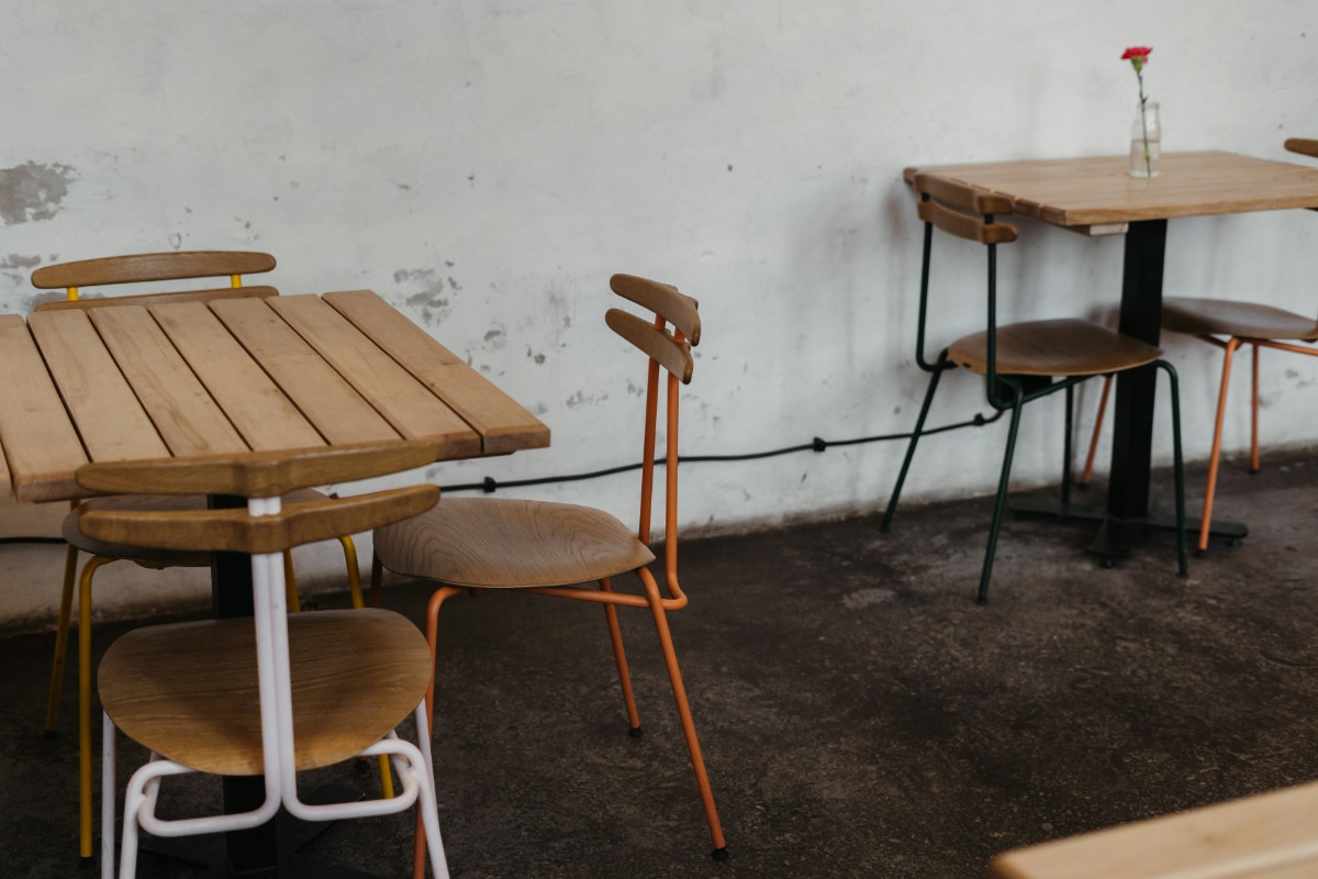 Two empty wooden tables with chairs in a cafe setting; one has a single flower in a vase.