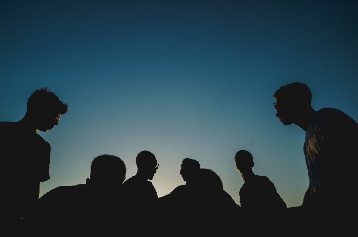 Silhouettes of six people against a clear blue sky at dusk.