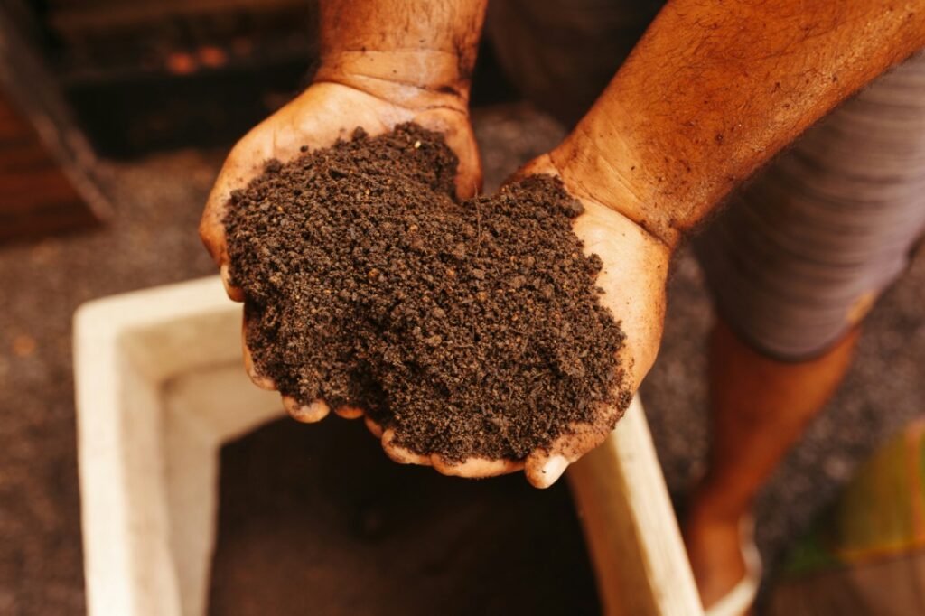 Hands holding a pile of dark soil over a container, with a blurred background.