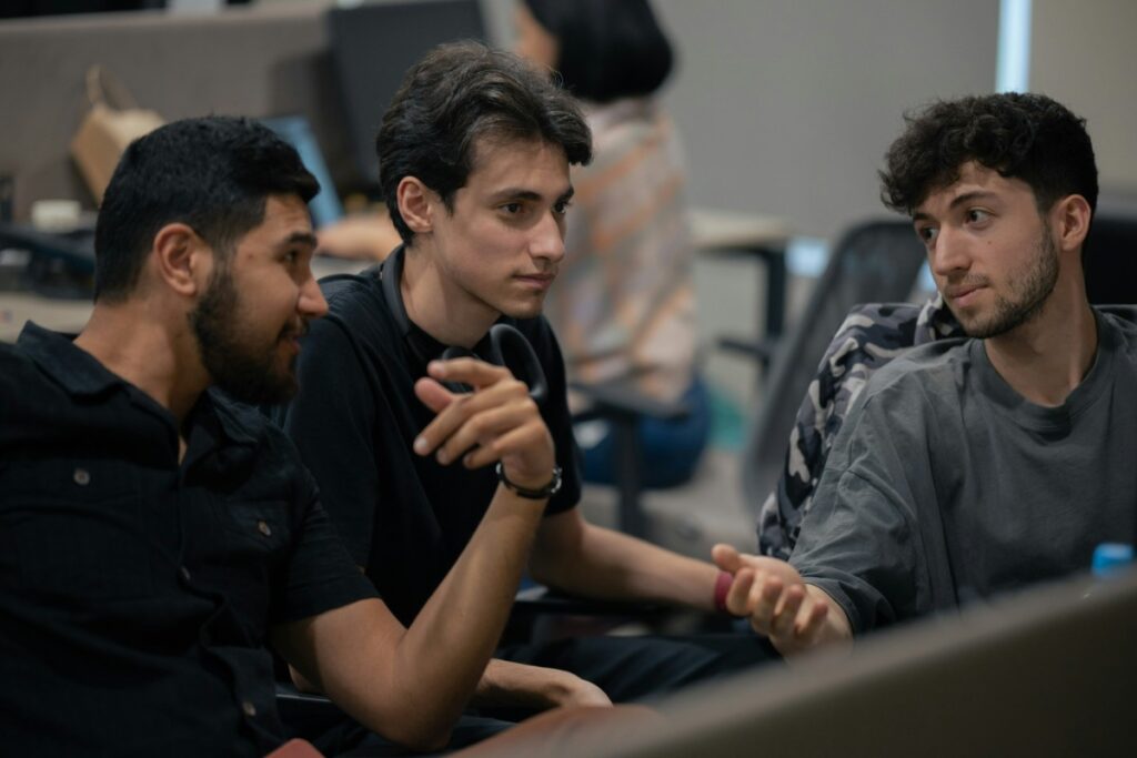 Three men are sitting and having a conversation in an indoor setting. The focus is on their interaction.
