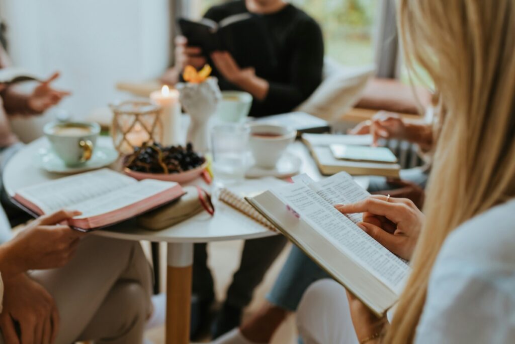 Group of people sit around a table with books and drinks, engaged in reading and discussion.