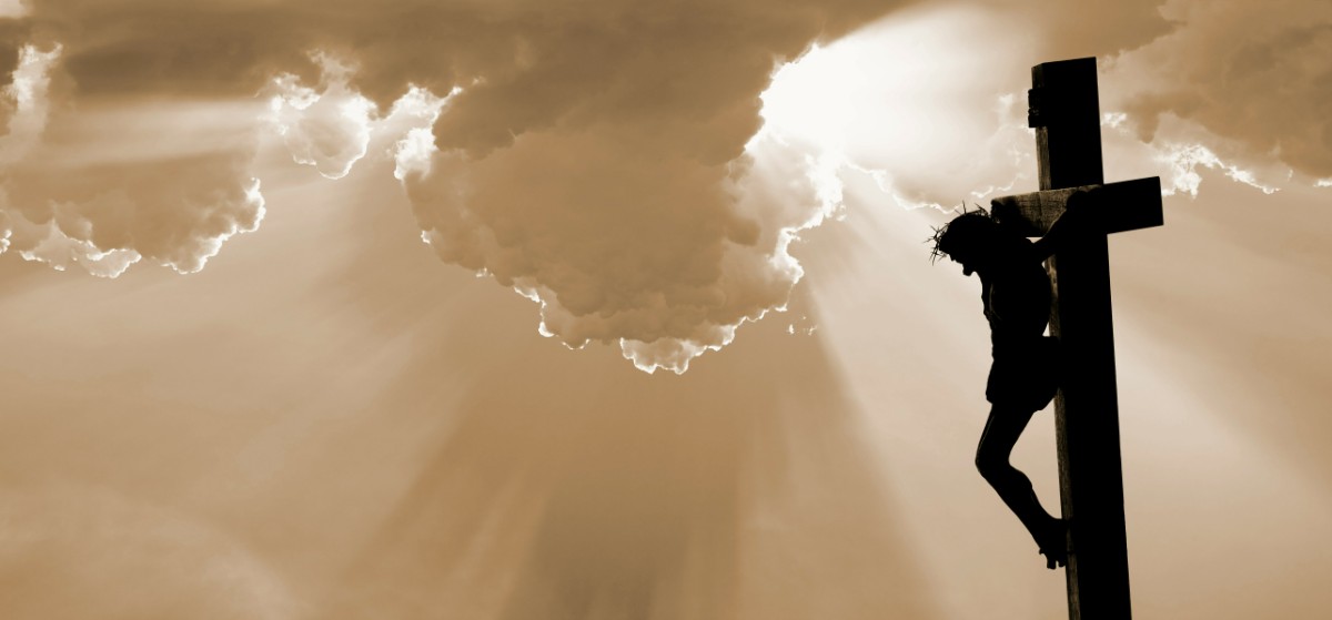 Silhouette of a person on a cross with dramatic rays of sunlight streaming through clouds in the background.