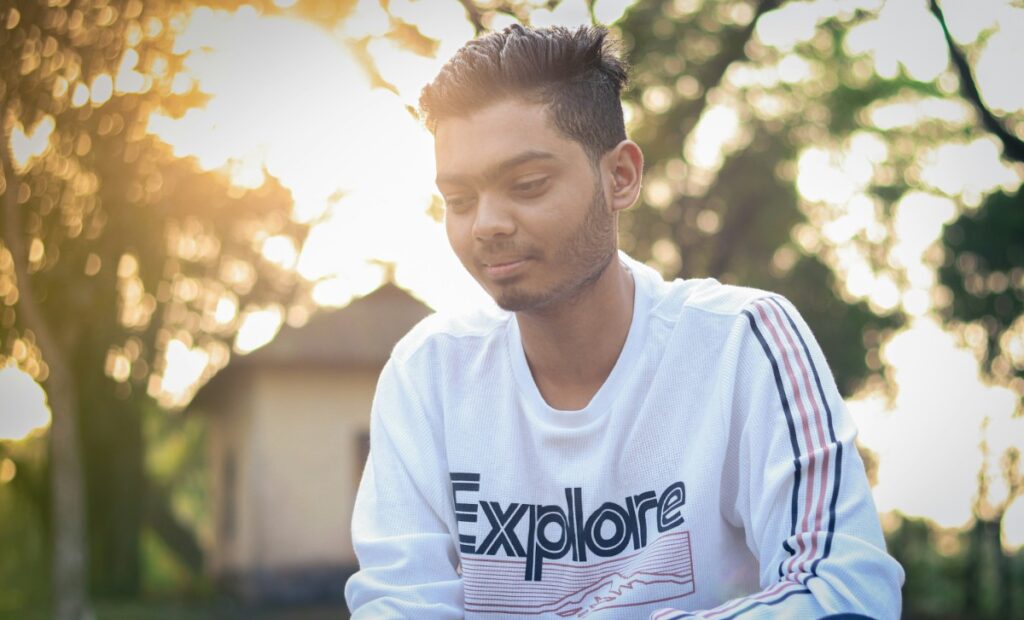 A person in a white Explore sweatshirt is sitting outdoors with trees and sunlight in the background.