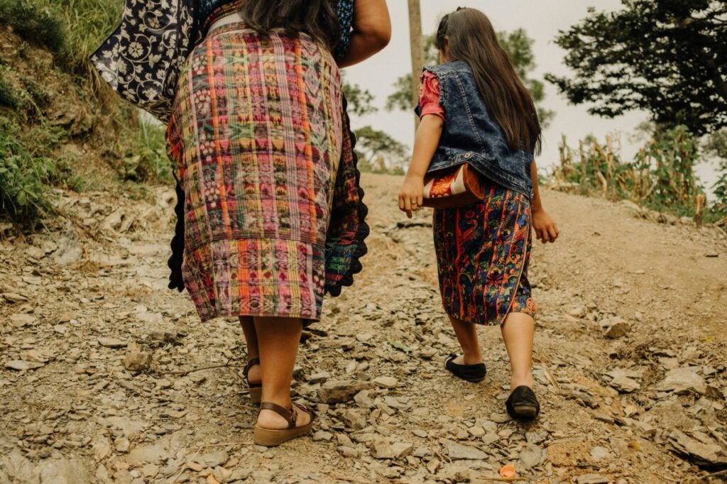 Two people in colorful traditional clothing walk up a rocky path surrounded by greenery.