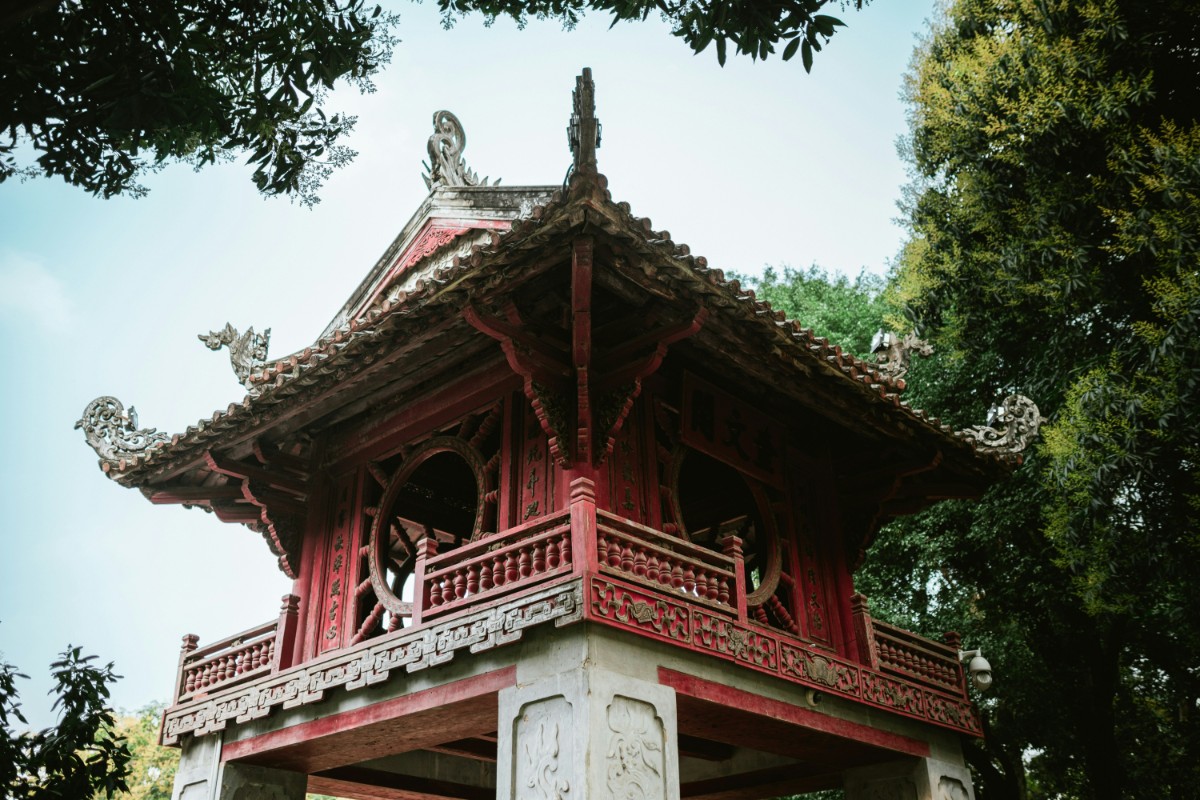 Traditional Asian pavilion with ornate roof and red wooden structure, surrounded by trees.