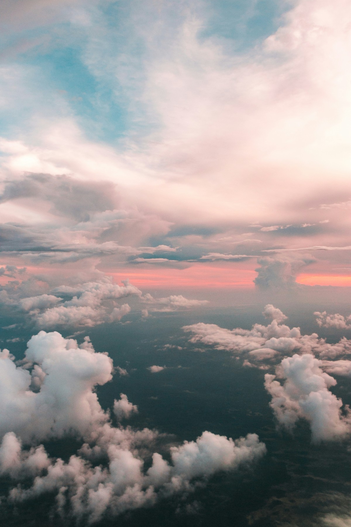 Aerial view of a sky with fluffy clouds, showing a mix of blue, pink, and orange hues during sunset or sunrise.