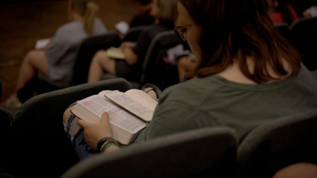 Women reading a Bible that has been highlighted and a journal next to it.