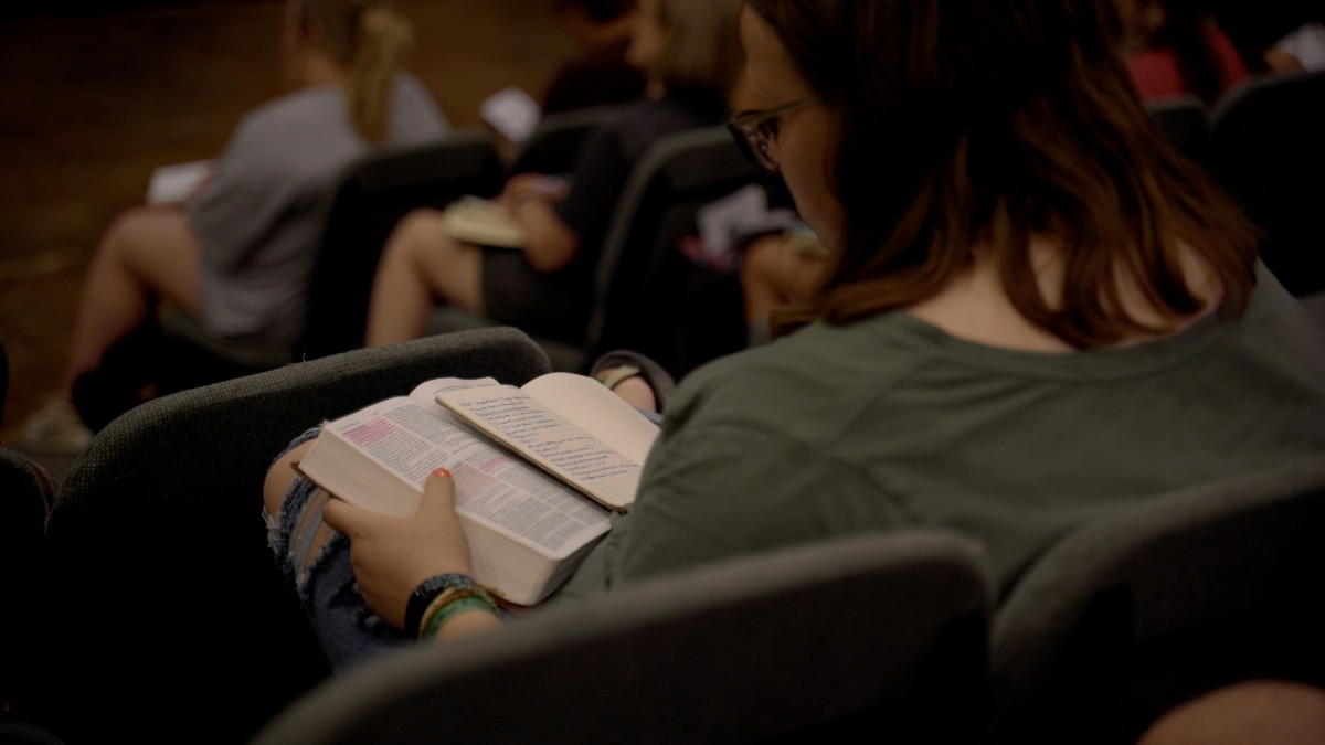Women reading a Bible that has been highlighted and a journal next to it.