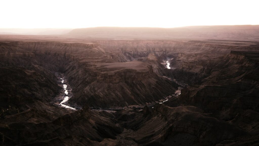 Aerial view of a deep canyon with a winding river at sunrise, surrounded by rugged terrain.
