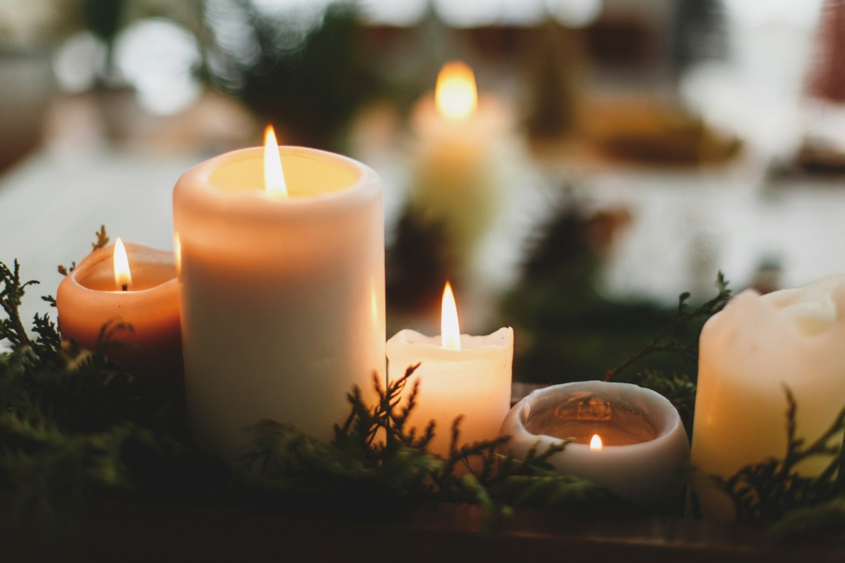 Several lit candles of varying sizes surrounded by greenery.
