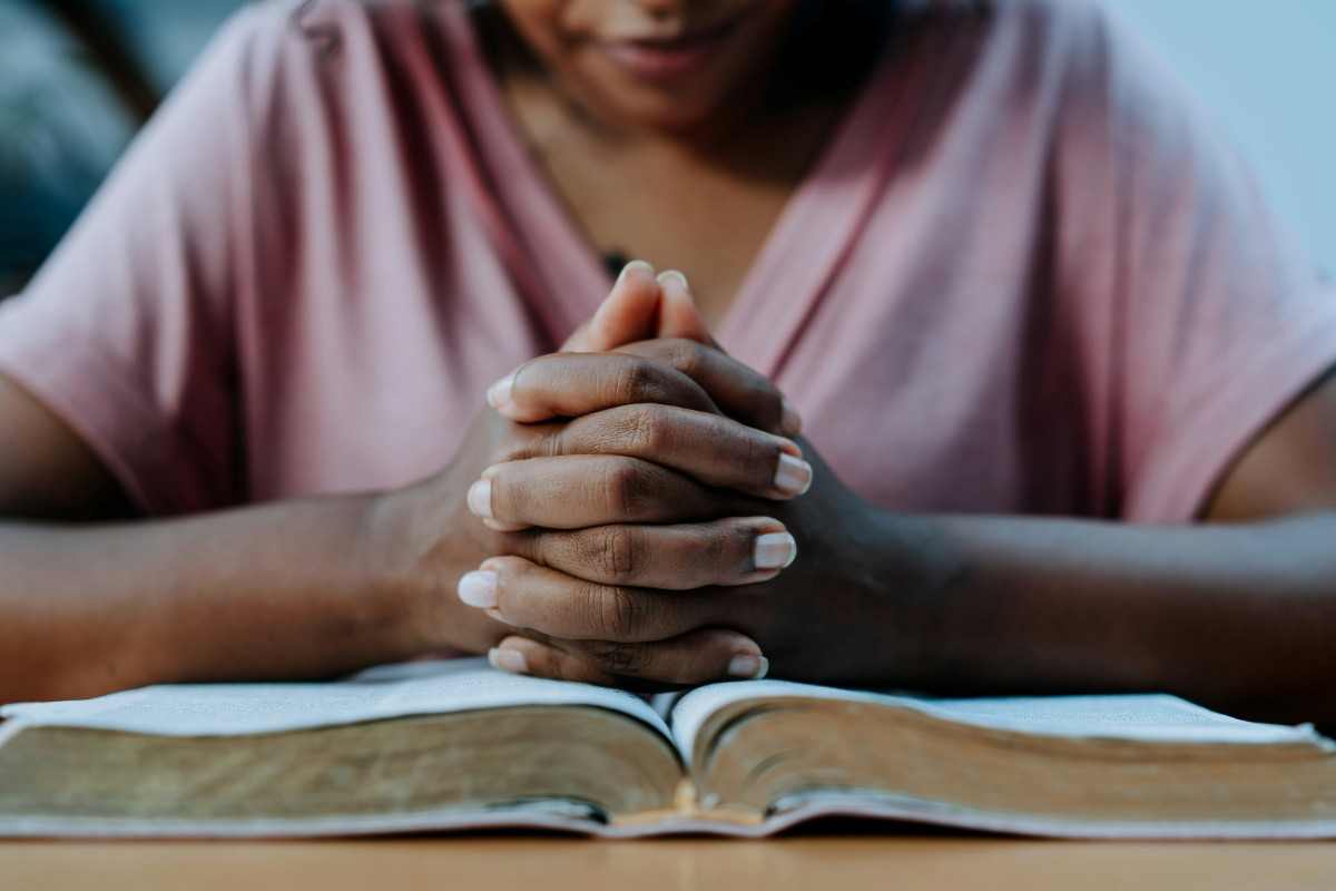 Person with clasped hands sits at a table with an open book.