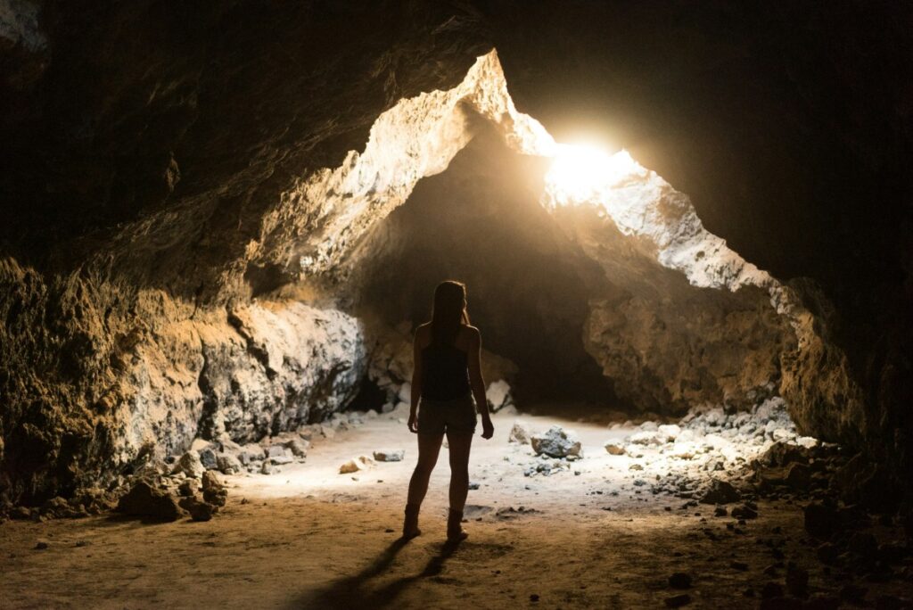Silhouette of a person standing inside a dimly lit cave, with sunlight streaming through the cave entrance.