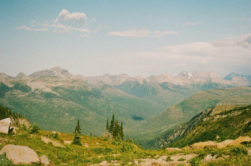 Mountain landscape with green valleys, distant rocky peaks under a blue sky with scattered clouds.