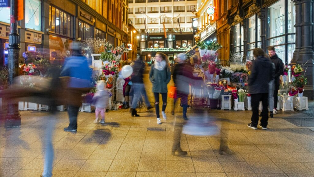 Blurry image of people walking by a market with flowers for sell.