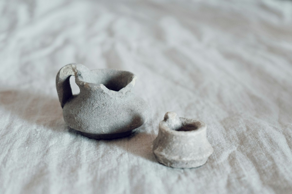 Two small, gray clay pots placed on a textured fabric surface.