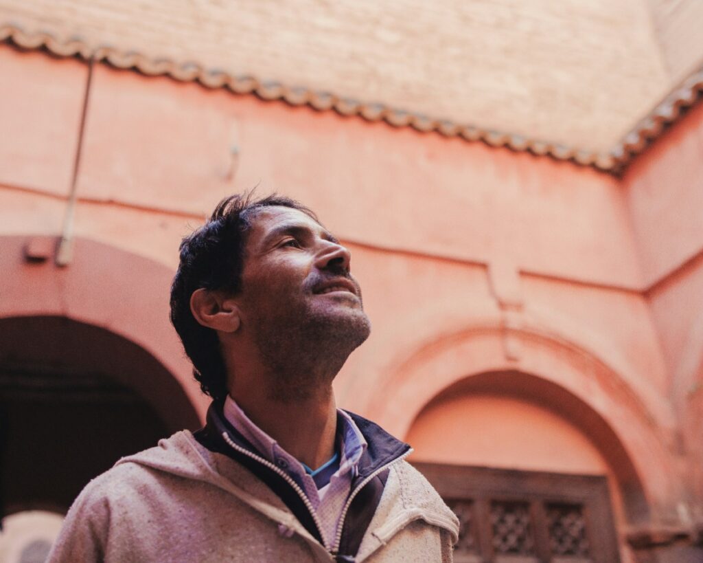 Man in casual clothing looks upwards while standing in a courtyard with red brick walls and arches.