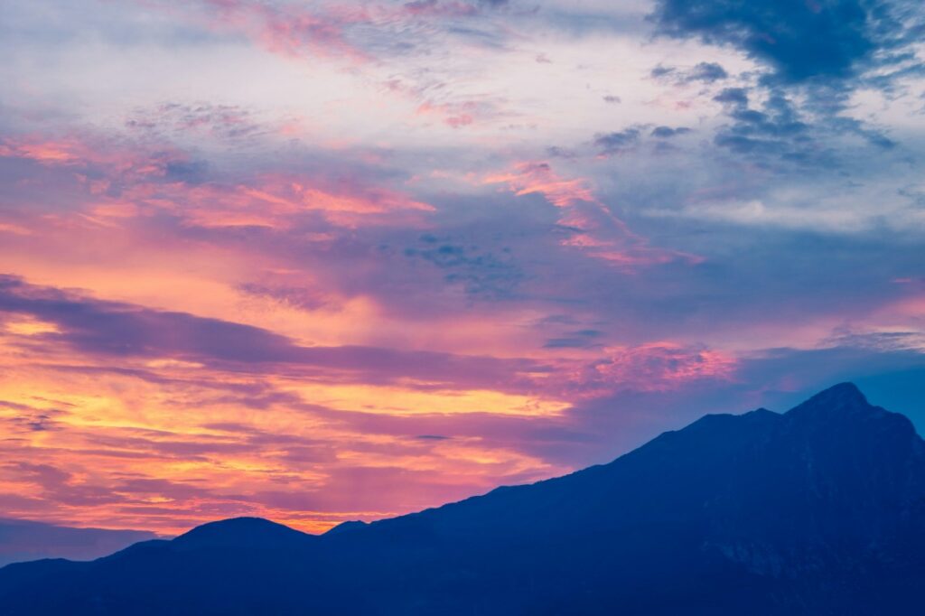 Colorful sunset sky with pink, orange, and blue hues over a silhouette of mountain peaks.