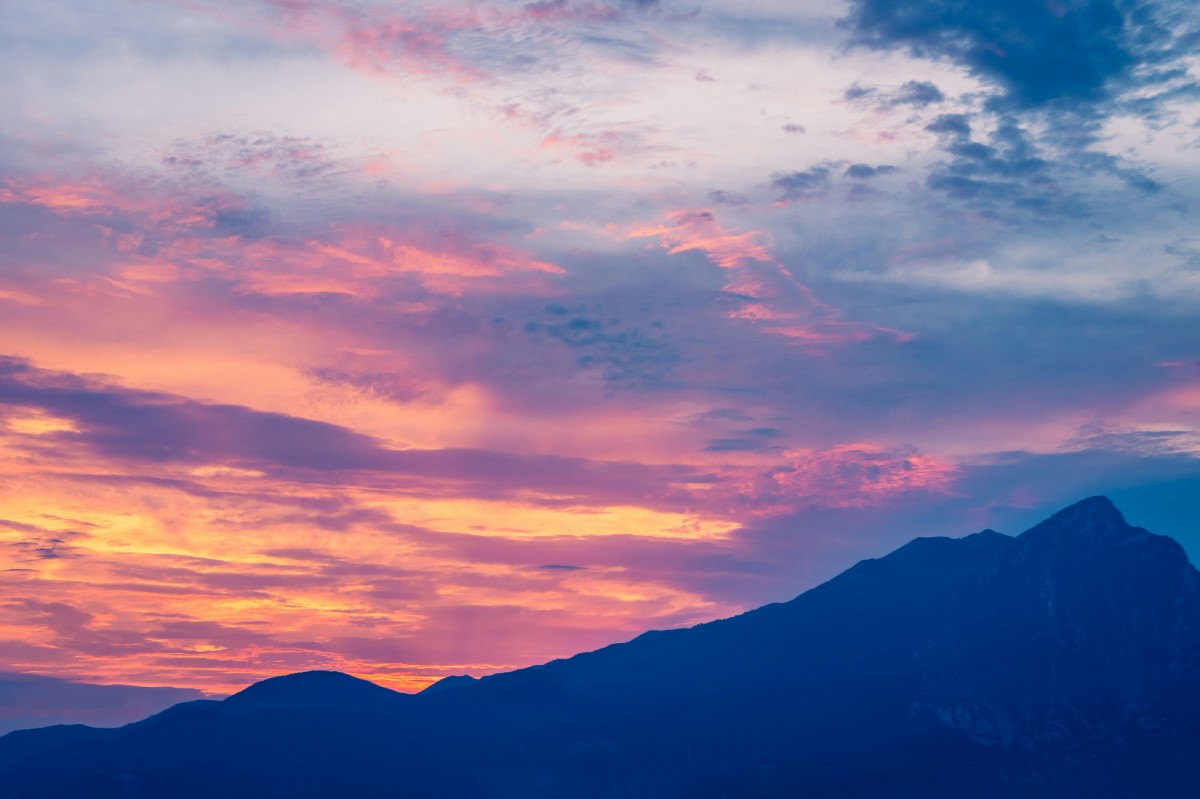 Colorful sunset sky with pink, orange, and blue hues over a silhouette of mountain peaks.
