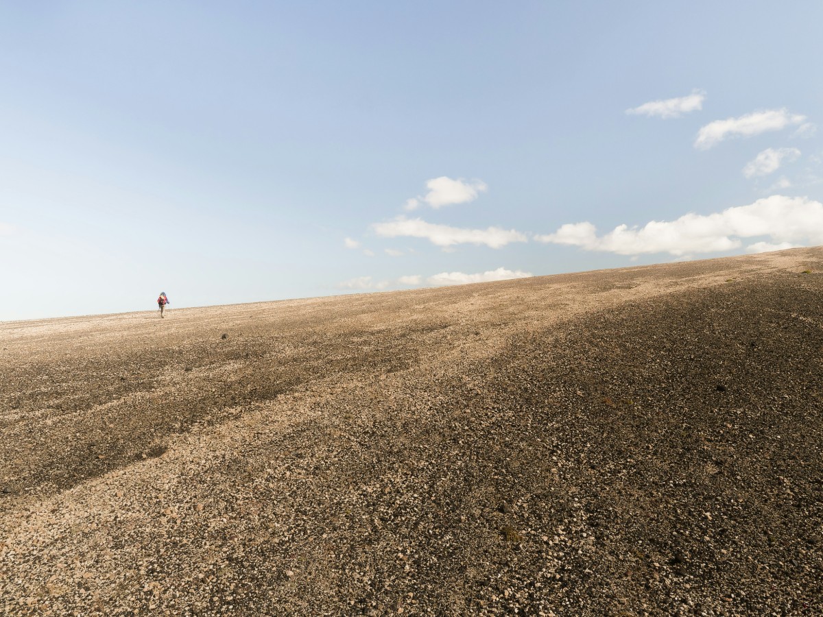 Empty Grass Field with a person hiking up the field under an open sky
