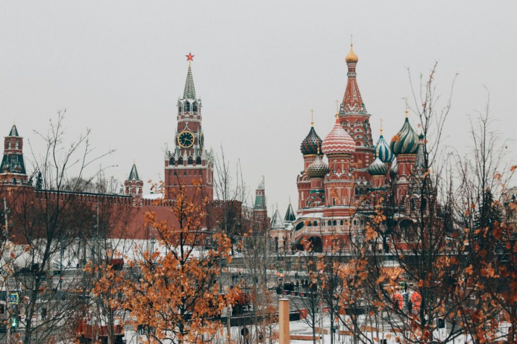 The image shows the Kremlin complex and St. Basils Cathedral in Moscow, with bare trees and a cloudy sky.