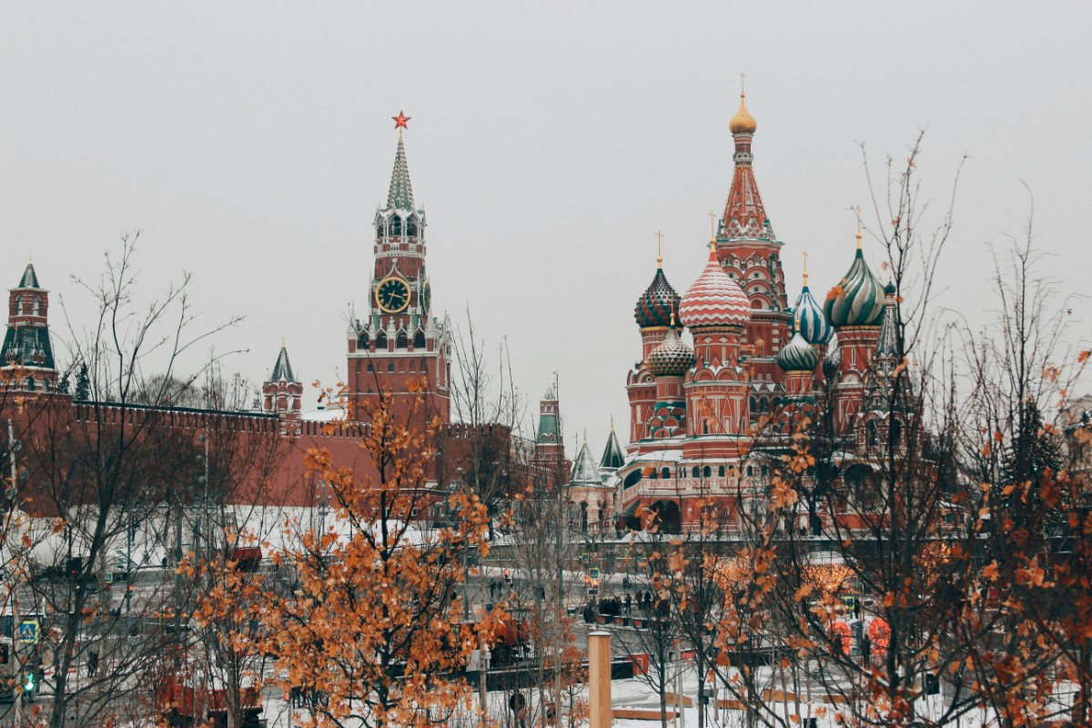 The image shows the Kremlin complex and St. Basils Cathedral in Moscow, with bare trees and a cloudy sky.