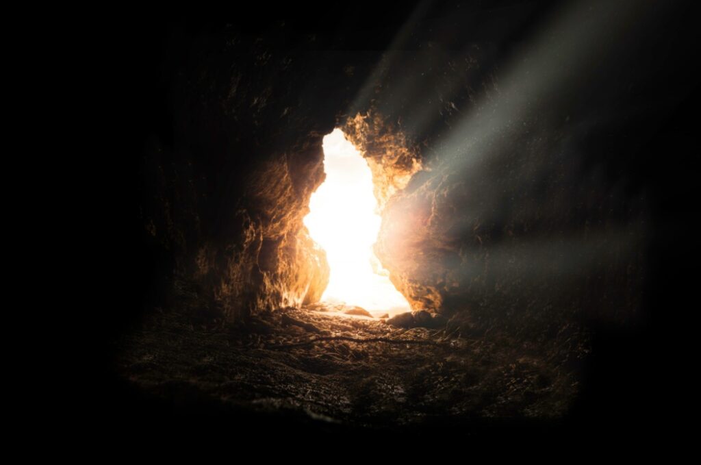 Sunlight streams through a cave opening, illuminating the rough, dark interior with a bright glow.