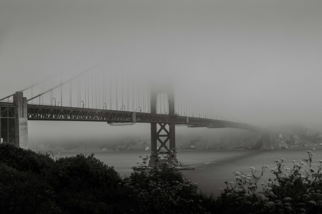 Foggy view of a large suspension bridge spanning across the water with the city barely visible in the background.