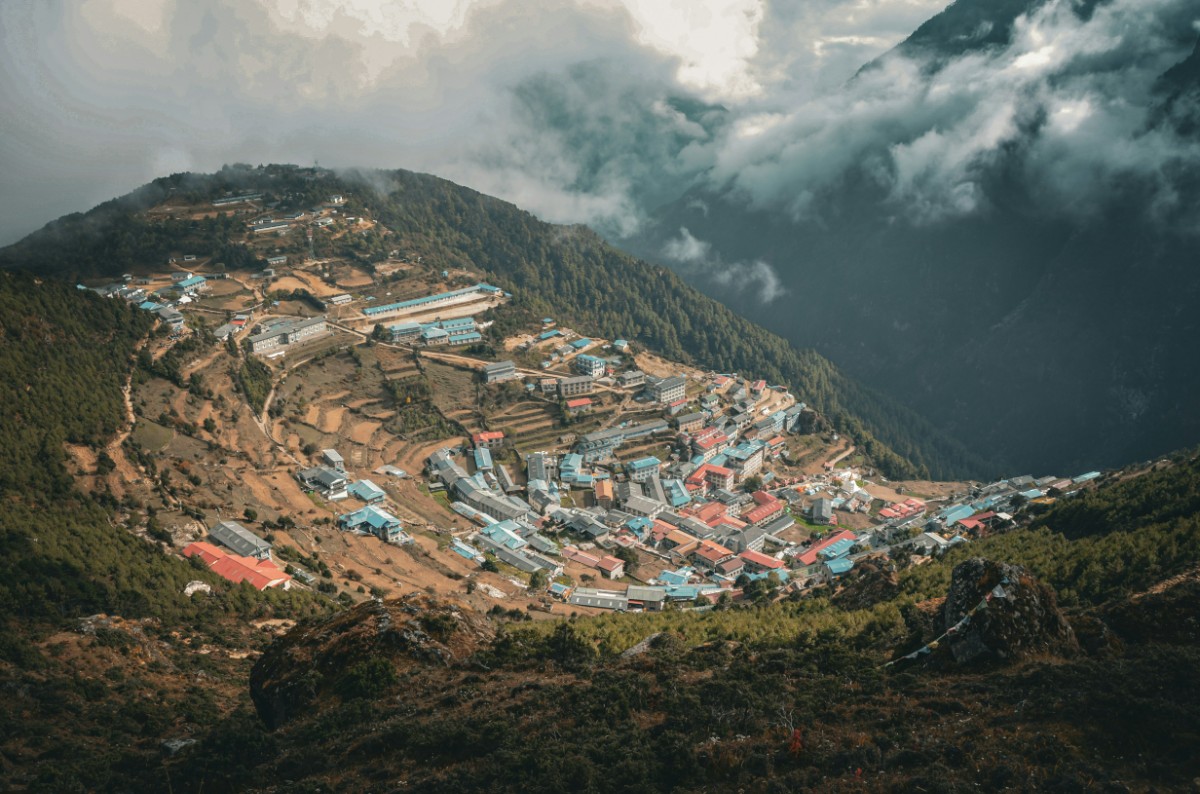 Aerial view of a village nestled in a mountainous valley, with clustered buildings and overcast skies.