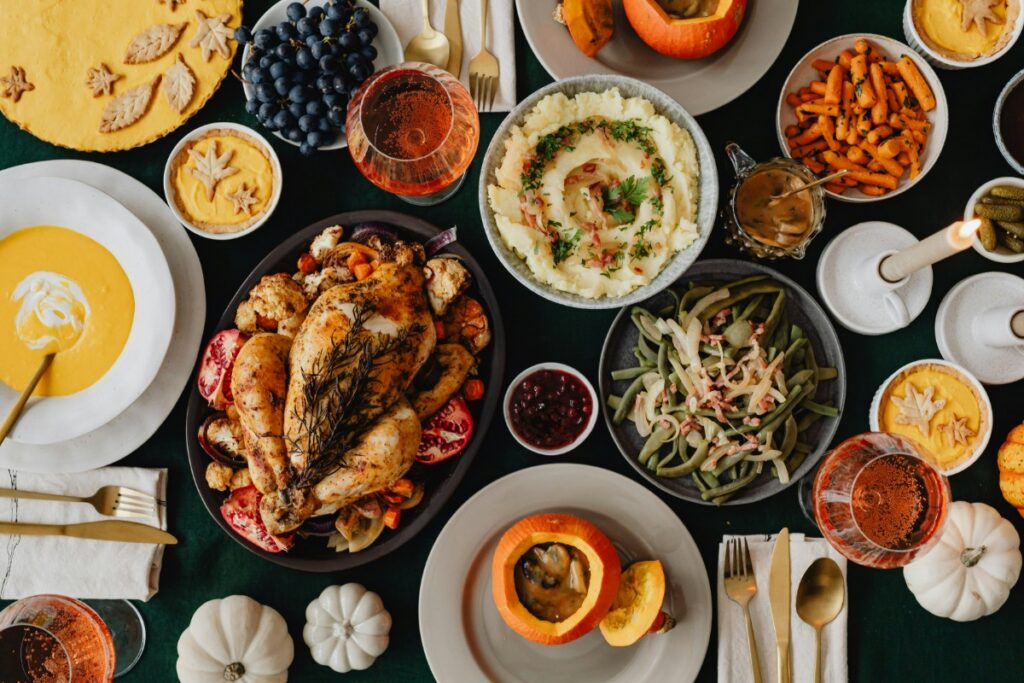 A table with a variety of dishes, including a roasted chicken, mashed potatoes, green beans, sweet potatoes, fruit, and drinks.