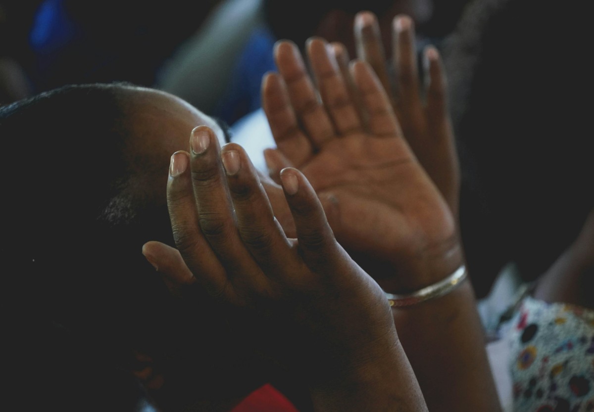 Hands raised in prayer, palms up, during a religious gathering.