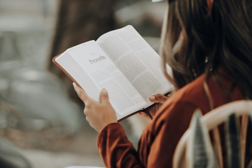 A person with long hair reads an open book while sitting on a chair, focusing on a page of text.