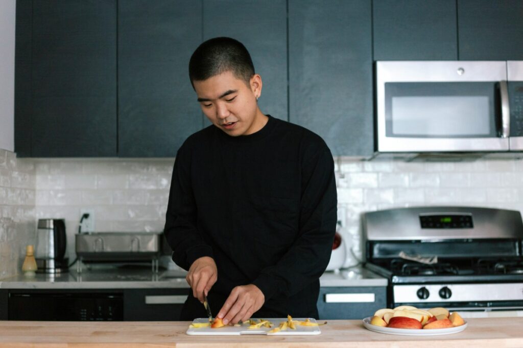 Person cutting fruit in a modern kitchen with black cabinets and stainless steel appliances.