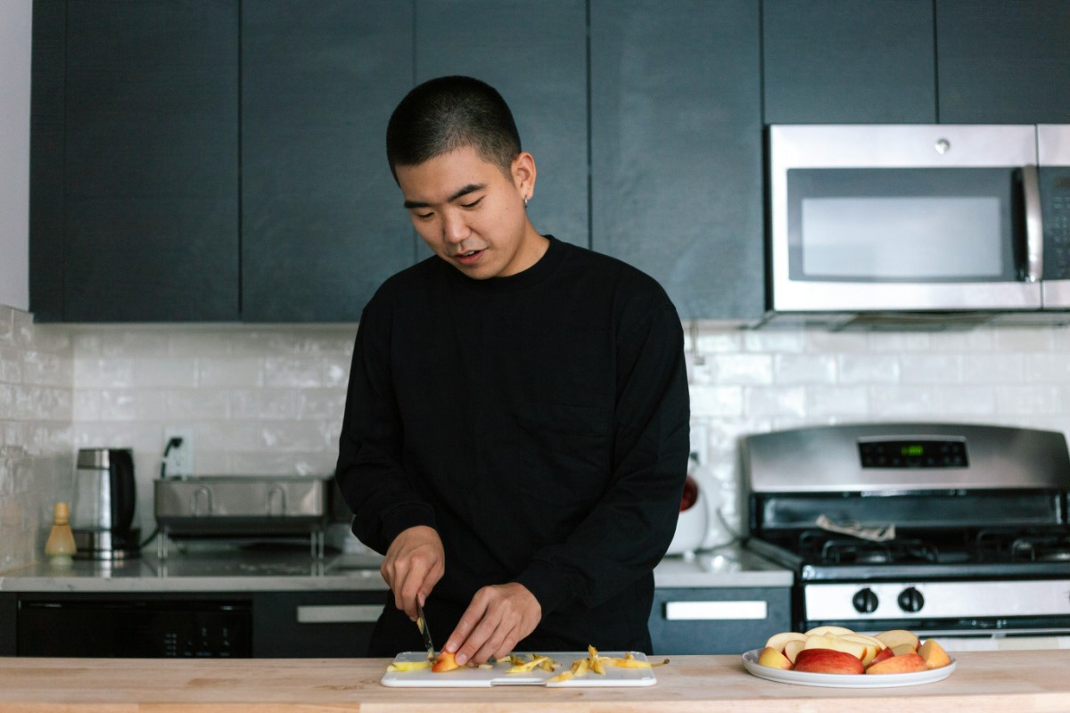 Person cutting fruit in a modern kitchen with black cabinets and stainless steel appliances.